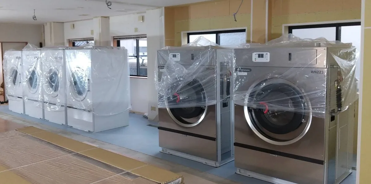 改装中の室内に搬入された、養生シート付きの業務用乾燥機と洗濯機